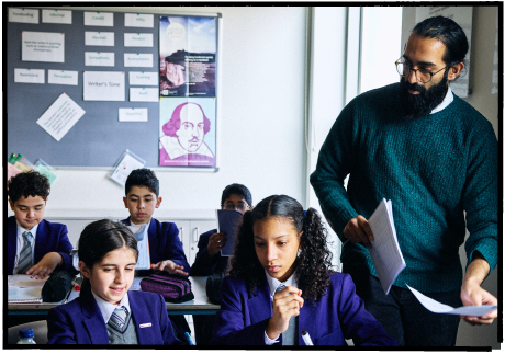 Photo of a teacher handing out worksheets to pupils in a classroom